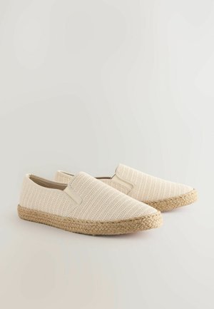Chaussures slip-on beiges avec une tige en tissu texturé, des accents élastiques et une semelle en jute tressé. Design léger et décontracté.