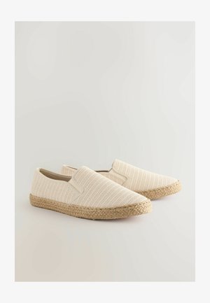Chaussures slip-on beiges avec une tige en tissu texturé, des accents élastiques et une semelle en jute tressé. Design léger et décontracté.
