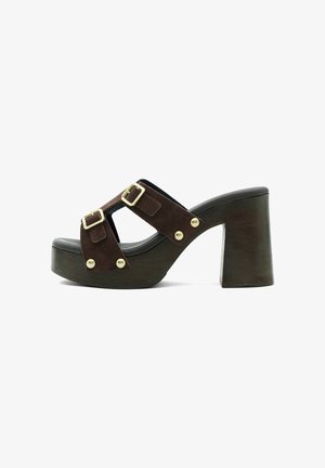 Sandale compensée en daim marron avec larges brides, boucles dorées et clous, avec un talon haut et épais et une semelle en bois.