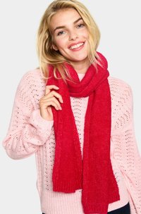 Rød tørklæde lavet af blødt, tekstureret materiale, draperet løst om halsen. Kombineret med en lyserød, strikket sweater med et blomstermønster.