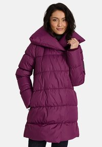 Violeta pūkaina mētelis ar augstu apkakli, kuram ir quilted raksts un redzami šuvumi. Materiāls izskatās gluds un spīdīgs.