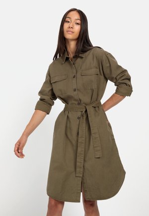 Khaki shirtjurk gemaakt van lichtgewicht stof, met een knoopsluiting aan de voorkant, twee borstzakken, lange mouwen en een strikceintuur.