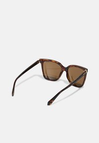 Sunglassit tortoiseshell-kannella lupaudun, kulmikkaalla muotoilulla ja kiiltävällä pinnalla. Varret ovat hoikat ja mustat, kultaisilla koristehinkeillä.