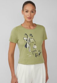 Olijf groene katoenen t-shirt met korte mouwen, met een zwart-wit grafische illustratie van twee figuren. Rond de hals en een aansluitend ontwerp.