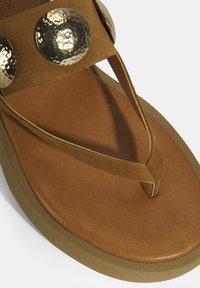 Braune Zehenstegsandalen mit einem weichen Fußbett, strukturierten Wildlederriemen und metallischen, gehämmerten Akzenten an den Riemen. Lässiges und leichtes Design.
