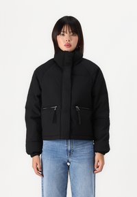 Svart cropped pufferjakke med høy krage, glidelåslommer foran og elastiske mansjetter. Glatt tekstur, minimalistisk design og uten mønstre.