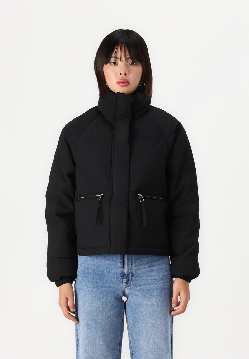 Svart cropped pufferjakke med høy krage, glidelåslommer foran og elastiske mansjetter. Glatt tekstur, minimalistisk design og uten mønstre.