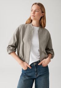 Giacca bomber grigia a spina di pesce con zip anteriore, vestibilità cropped e maniche arricciate, abbinata a una maglietta bianca e jeans a vita alta.