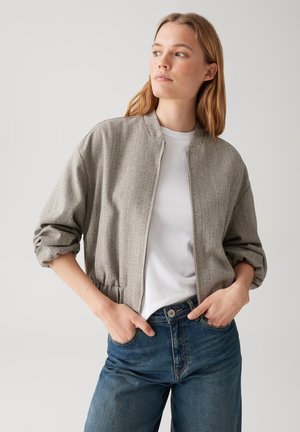 Giacca bomber grigia a spina di pesce con zip anteriore, vestibilità cropped e maniche arricciate, abbinata a una maglietta bianca e jeans a vita alta.