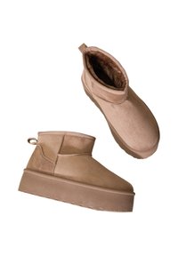 Bottes de cheville en suède beige avec une doublure intérieure douce, semelle plate et talon arrière. Présente un design simple et épuré.