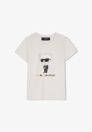 Kremfarvet t-shirt med en tegneseriefigur iført sorte solbriller og jakkesæt, med teksten "KARL LAGERFELD" nedenunder i guld bogstaver.
