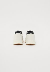 White athletic shoes with a black heel collar, textured rubber outsole, smooth upper material, and minimalistic design.