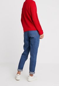 Röd ribbad tröja, lösa mörkblå jeans med uppvikta benslut och vita sneakers. Enkelt mönster med synlig sömnad och fickor.