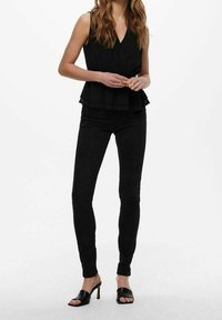 Top peplum nero con scollo a V, design a strati. Jeans neri aderenti e mule neri con tacco. Tessuto liscio, silhouette elegante.
