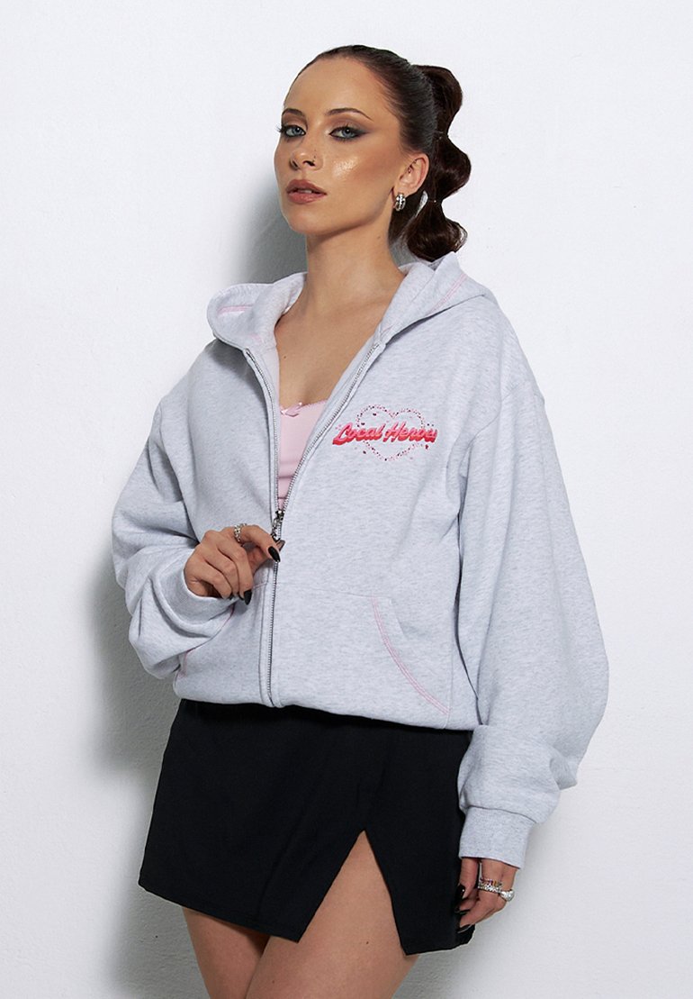 Szara bluza z zamkiem błyskawicznym i różowymi akcentami, z haftowanym napisem "Local Honey". Połączona z czarną mini spódnicą i różową bluzką pod spodem.