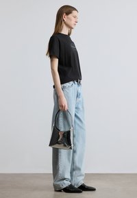 Μαύρο μπλουζάκι με λογότυπο, ανοιχτό μπλε τζιν ψηλόμεσο, και γυαλιστερή μαύρη τσάντα. Η μοντέλο φοράει μυτερά μαύρα μποτάκια αστραγάλου.