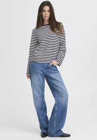 Triibuline pikkade varrukatega tumesinine ja beež ülaosa, kombineeritud laia säärega siniste teksadega. Teksad on heledama pesuga ja klassikalise viie taskuga disainiga.