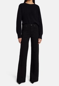 Suéter negro de punto acanalado y jeans negros de cintura alta, con un corte de pierna ancha y tacones de punta negros. Textura suave y diseño clásico.