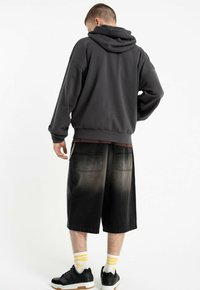 Ciemnoszara bluza z kapturem na sznurki, w połączeniu z czarnymi szortami dżinsowymi z efektem wyblaknięcia oraz czarnymi trampkami w towarzystwie skarpet w białe i żółte paski.