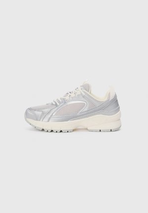 Silver athletic sneaker with a mesh upper and reflective accents. Cream rubber sole and laces; designed with a sleek, rounded shape.
