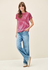 Camiseta gráfica rosa y marrón con mangas cortas, combinada con jeans de pierna ancha en azul claro y zapatos beige. Diseño simple con detalles en texto.
