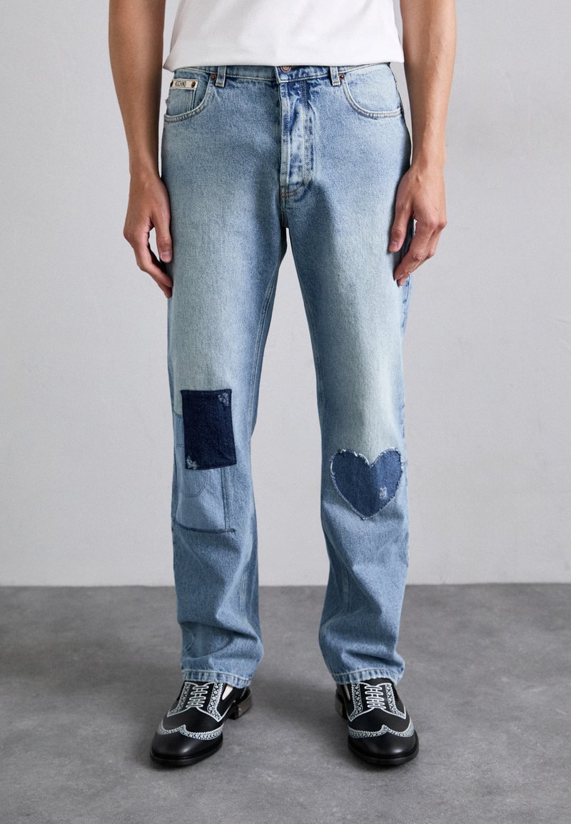 Light blue denim jeans with distressed patches; dark blue square and heart-shaped accents. Straight leg design, mid-rise fit.