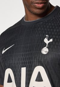 Maillot de football noir avec un motif texturé. Présente un logo Nike blanc, "AIA" en grandes lettres, et un écusson des Spurs avec un oiseau et un ballon.