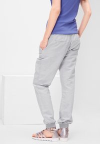 Pantalons de jogging gris clair en tissu doux avec un waistband élastique et des poignets élastiques. Dotés de deux poches arrière, associés à des sandales à lanières argentées.