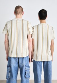 T-shirts rayés en crème et beige, avec des manches courtes, un col rond et une coupe décontractée, associés à un pantalon cargo bleu.