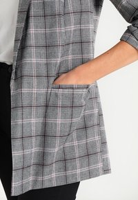 Károvaný blejzr v šedé, bílé a růžové barvě. Disponuje jednou přední kapsou a má upravený střih s ohrnutými rukávy. Měkká tkanina a strukturovaný design.