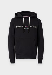 Zwarte hoodie van een katoenmix met een voorzak in kangoeroestijl, witte trekkoorden en het "TOMMY HILFIGER" logo in het wit gedrukt over de borst.