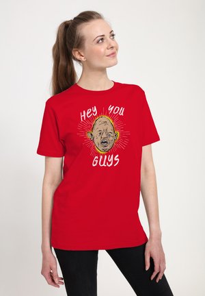 Unge kvinde med hestehale iført en rød T-shirt med et tegneserieansigt og teksten "Hey You Guys" i hvide bogstaver.