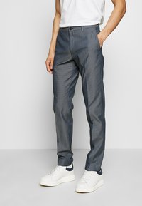 Přizpůsobené kalhoty tmavě modré barvy s vzorem a hladkou texturou, se slim fit střihem, bočními kapsami a malým knoflíkovým zapínáním. Spárováno s bílými teniskami.