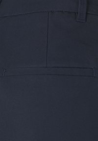 Detalle del bolsillo trasero de unos pantalones azul marino oscuro con costuras visibles y presilla de cinturón sobre el bolsillo.