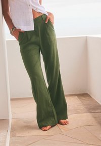 Pantalon large en lin vert avec un devant plissé et des poches latérales. Caractérisé par une taille haute et une coupe décontractée, idéal pour un look casual.