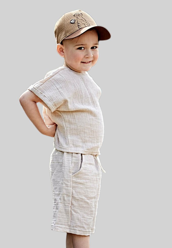 Hellbeigees Leinenoutfit mit einem kurzärmligen Oberteil und knielangen Shorts, mit einem Kordelzugbund und seitlichen Taschen. Braune Baseballmütze mit Design.