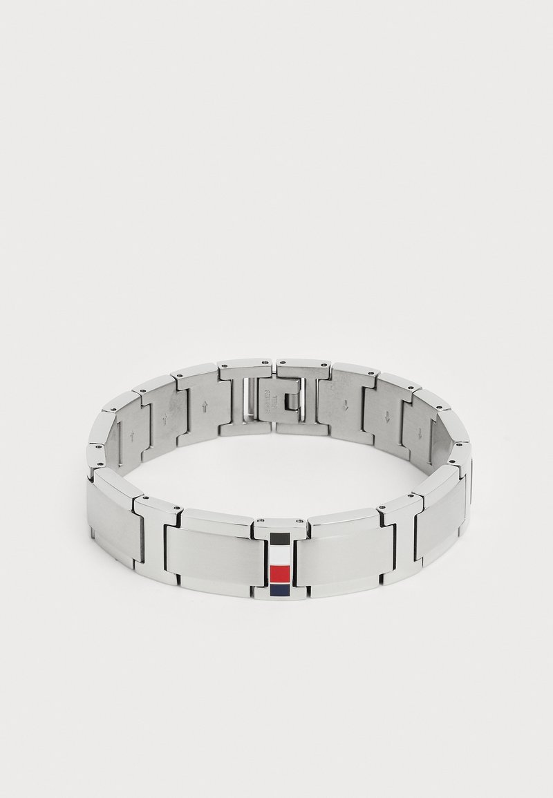 Bracciale in metallo con maglie intrecciate, caratterizzato da una finitura in argento lucido e spazzolato. Piccole decorazioni rosse, bianche e blu su una chiusura.