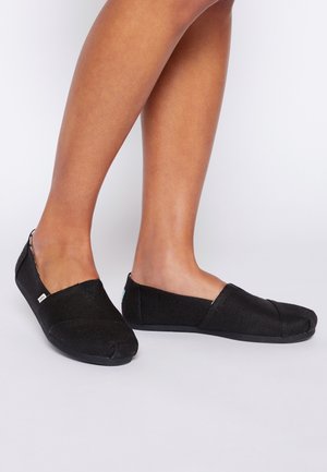Schwarze Canvas-Slipper mit strukturiertem Stoff, Gummisohle und einem niedrig geschnittenen Design. Verfügt über einen dezenten Logo-Akzent an der Ferse.