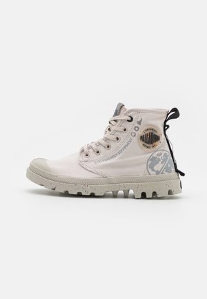 Light beige eco-friendly ankle boots with a rubber toe cap, textured speckled sole, and side logo detailing. Lace-up design with rear pull tab.