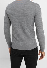 Gray knitted sweater with long sleeves and a round neckline. Features a textured fabric and fitted cuffs. Worn with dark jeans.