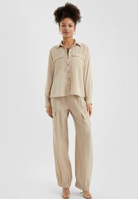 Beige button-down shirt met twee borstzakken, gecombineerd met losse cargo broek met elastische manchetten en een gestructureerde stof.