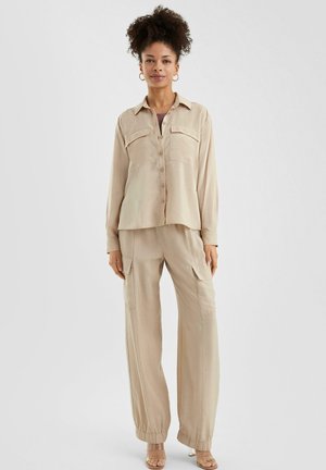 Beige button-down shirt met twee borstzakken, gecombineerd met losse cargo broek met elastische manchetten en een gestructureerde stof.