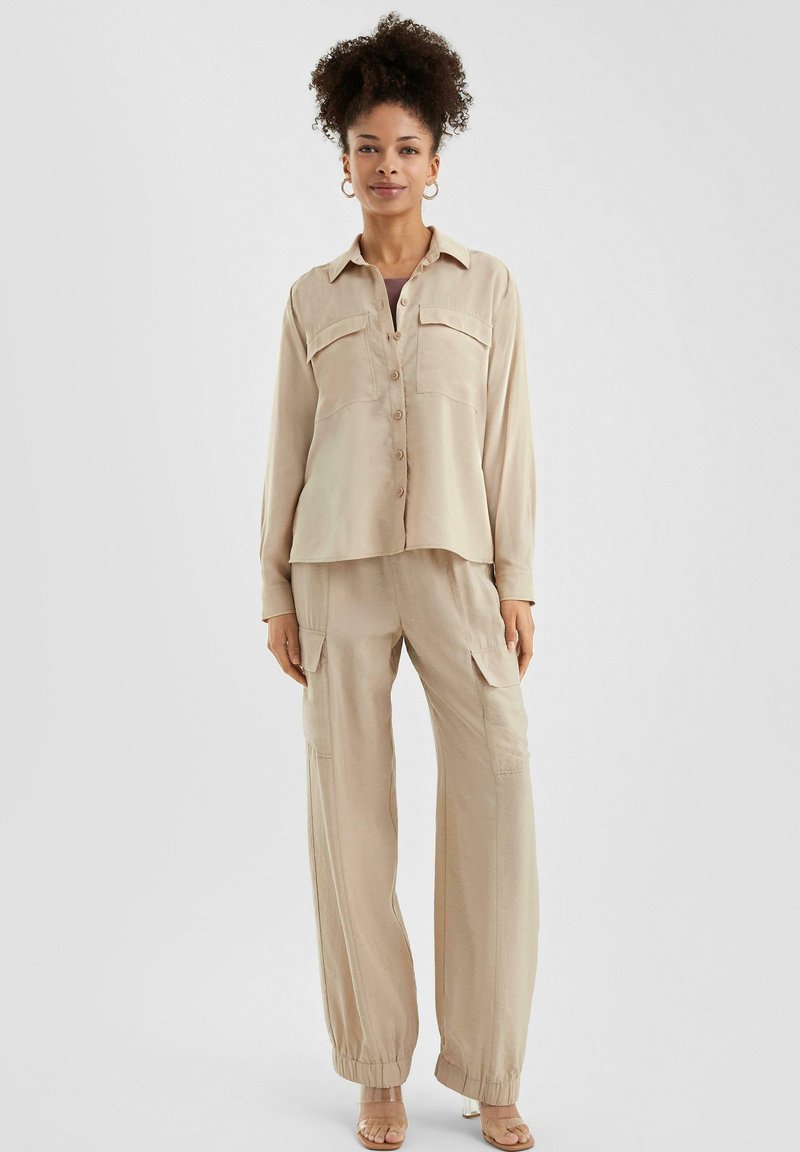 Beige button-down shirt met twee borstzakken, gecombineerd met losse cargo broek met elastische manchetten en een gestructureerde stof.