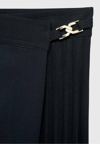 Vêtement noir avec une texture plissée, doté d'un fermoir en métal doré à la taille. Le tissu doux et le design ajusté sont visibles.