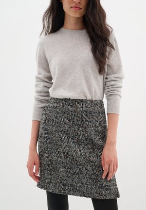 Pull gris clair à manches longues, associé à une jupe à motif en chevrons noir et blanc avec des éclats de couleur, longueur genoux.