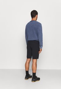 Sininen swetari pyöreällä kaula-aukolla ja rannekainaloilla, yhdistetty tummiin shortseihin. Mustat kengät ja sukat täydentävät asukokonaisuuden. Näyttää takaa.