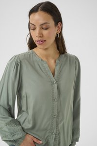Blusa button-up verde chiaro con maniche lunghe, rifinita con un pizzo decorativo lungo la placca e i polsini, realizzata in un tessuto morbido.