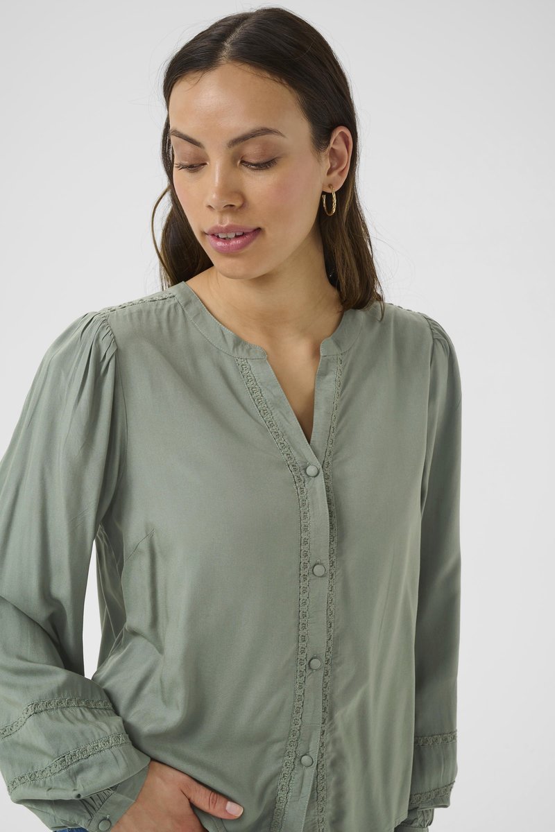 Blusa button-up verde chiaro con maniche lunghe, rifinita con un pizzo decorativo lungo la placca e i polsini, realizzata in un tessuto morbido.