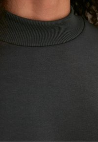 Suéter de cuello alto en gris oscuro con una tela suave y lisa y un collar de canalé. La textura es elástica con un diseño ajustado.