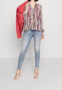 Rød suedjakke, mønstret bluse med lodrette striber i rød, sort og creme, slidte lyseblå skinny jeans og beige strophæle.